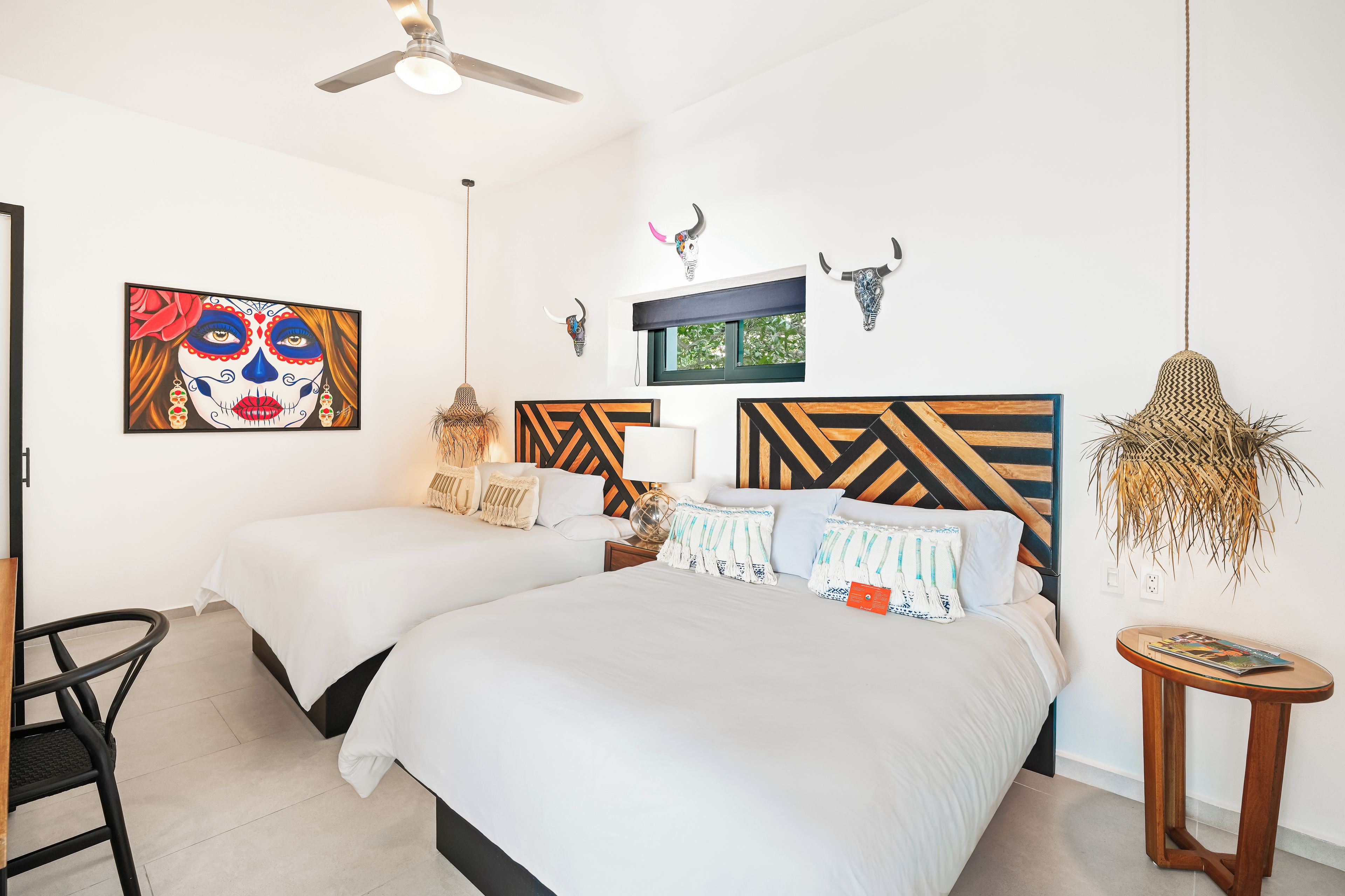Habitación de hotel con dos camas, ventilador de techo, ventana con vistas y decoración en la pared.