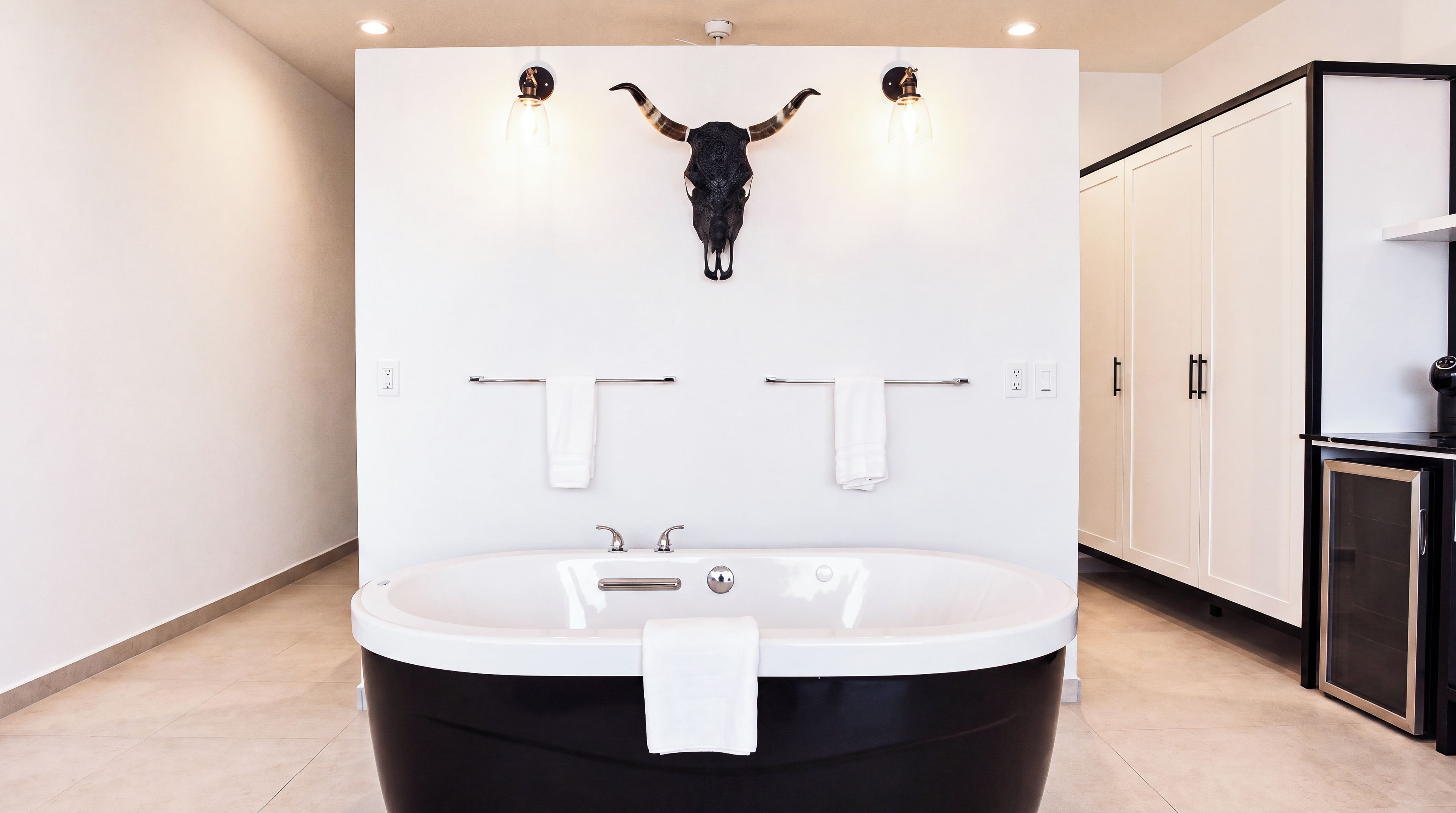 A modern bathroom with a large bathtub, two towel racks, and a wall-mounted light fixture above the bathtub.