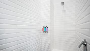Rincón de un baño con paredes de azulejos blancos y una ducha. Hay dos botellas de champú y acondicionador en un dispensador de pared.
