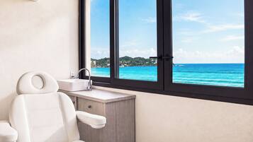A bathroom with a white bathtub, a sink, and a window with a view of the ocean.
