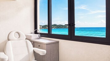 Un baño con una bañera blanca, un lavamanos y un ventanal con vista al océano.