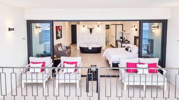 A modern interior with a living area, a large bed, a bathtub, and a view through a glass door.