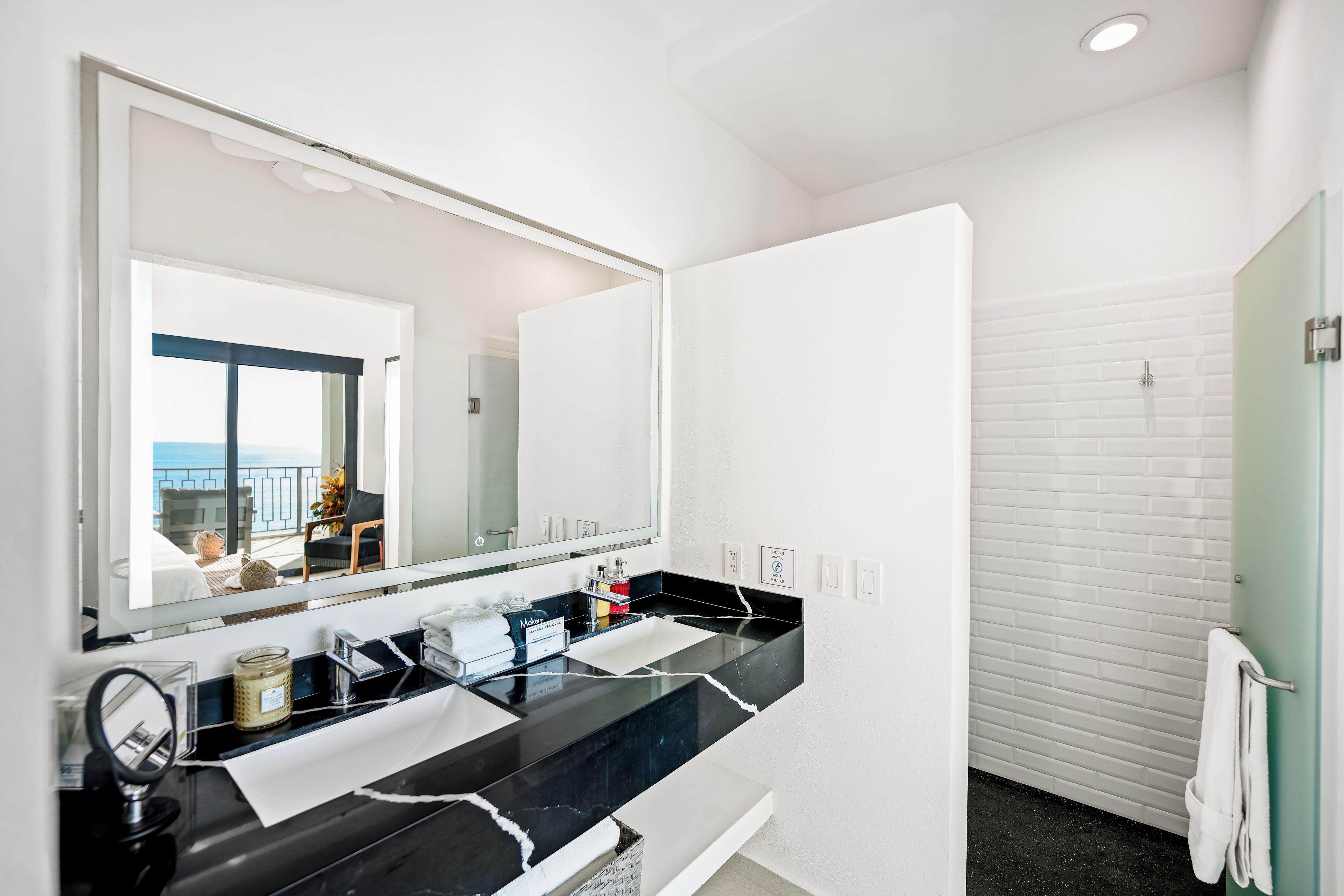 A modern bathroom with a black marble countertop, a large mirror, and a visible towel rack.