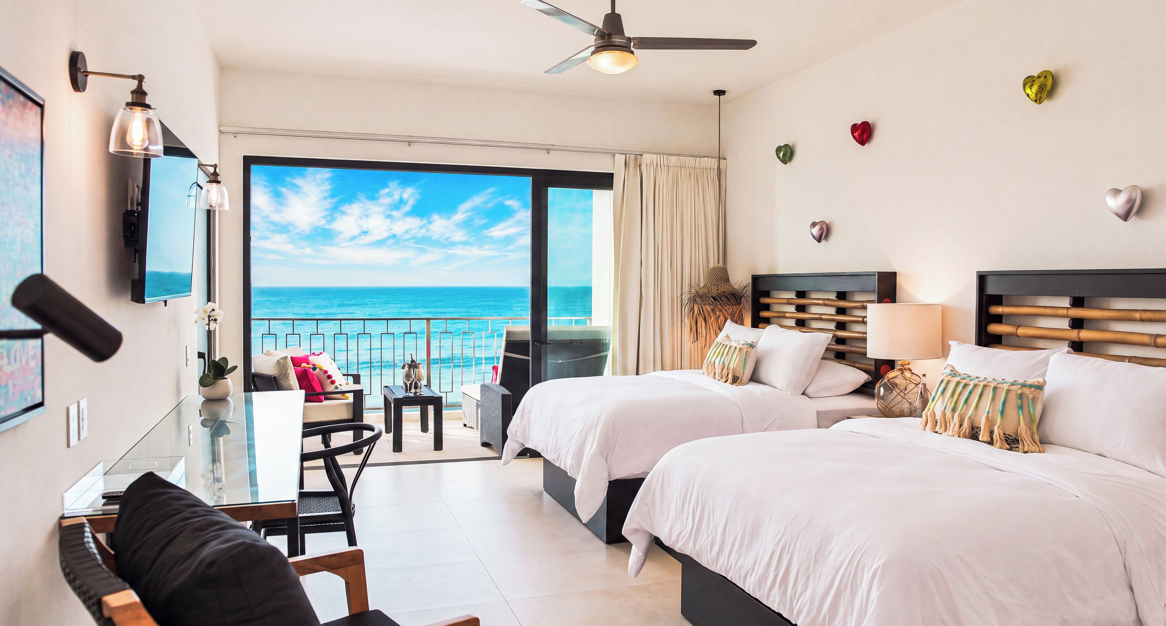 Habitación de hotel con balcón, dos camas, escritorio y televisor.