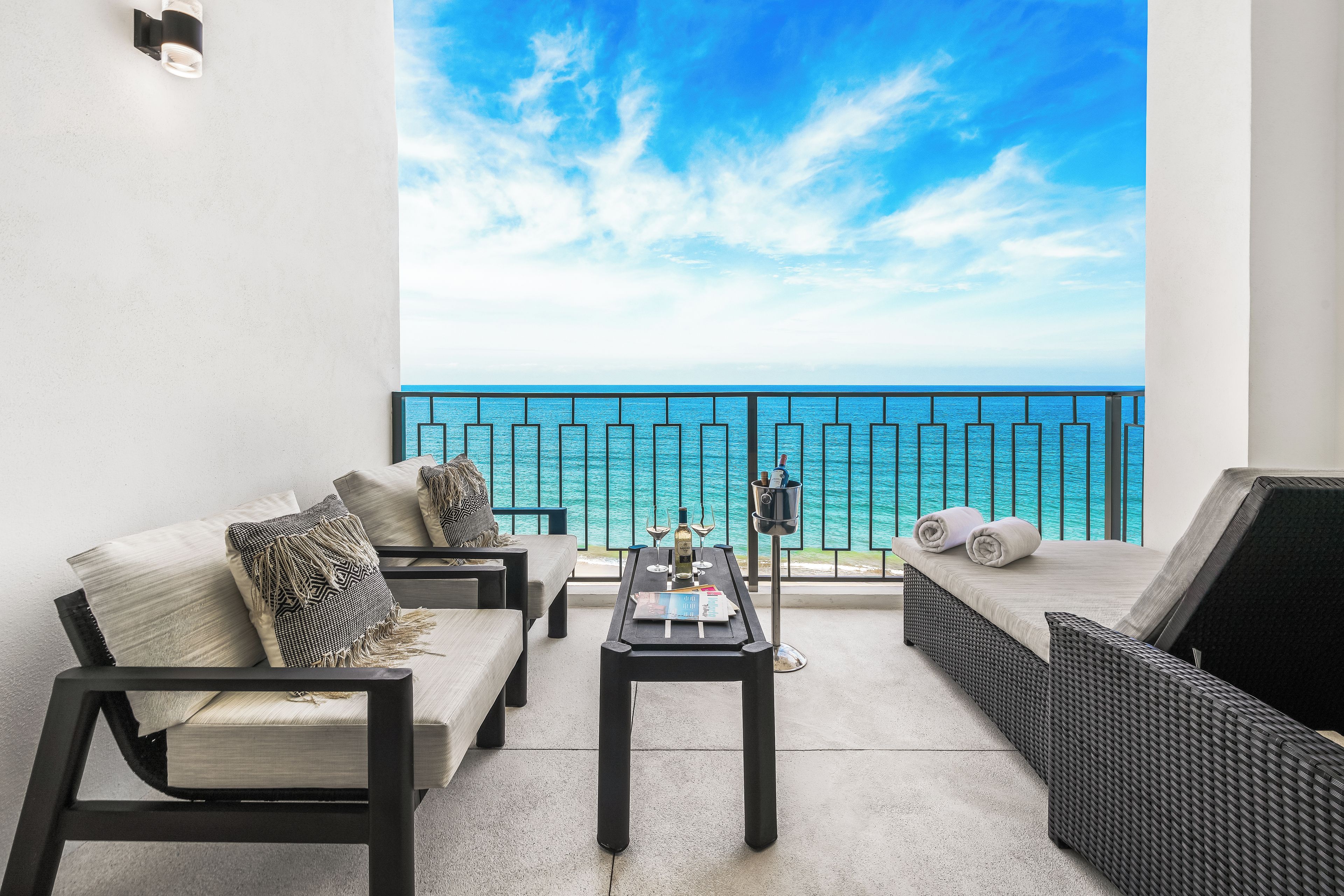 A balcony with a view of the sea, furnished with a sofa, chairs, and a table.