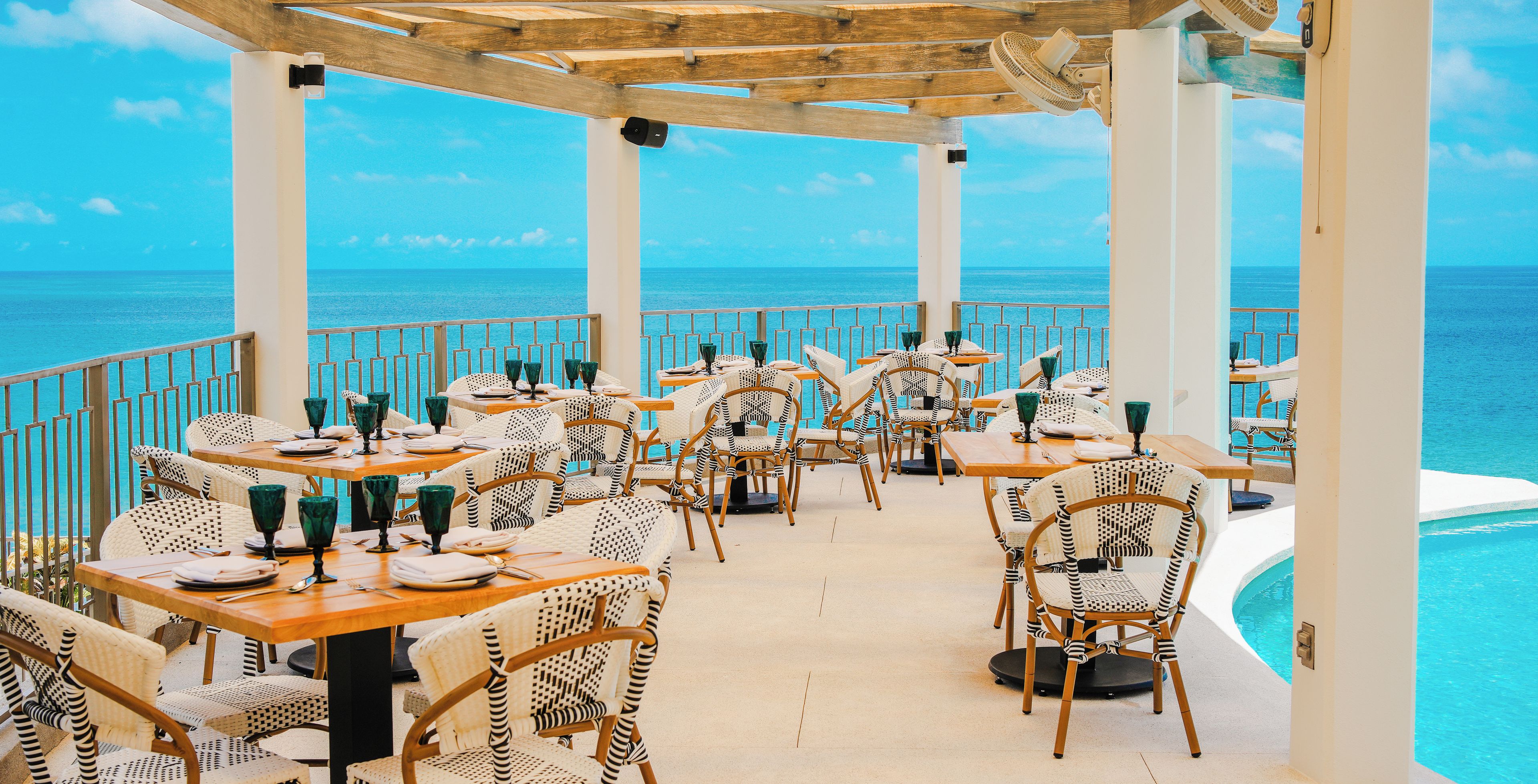 Un área de comedor al aire libre con mesas y sillas, con vista a una piscina y al mar.