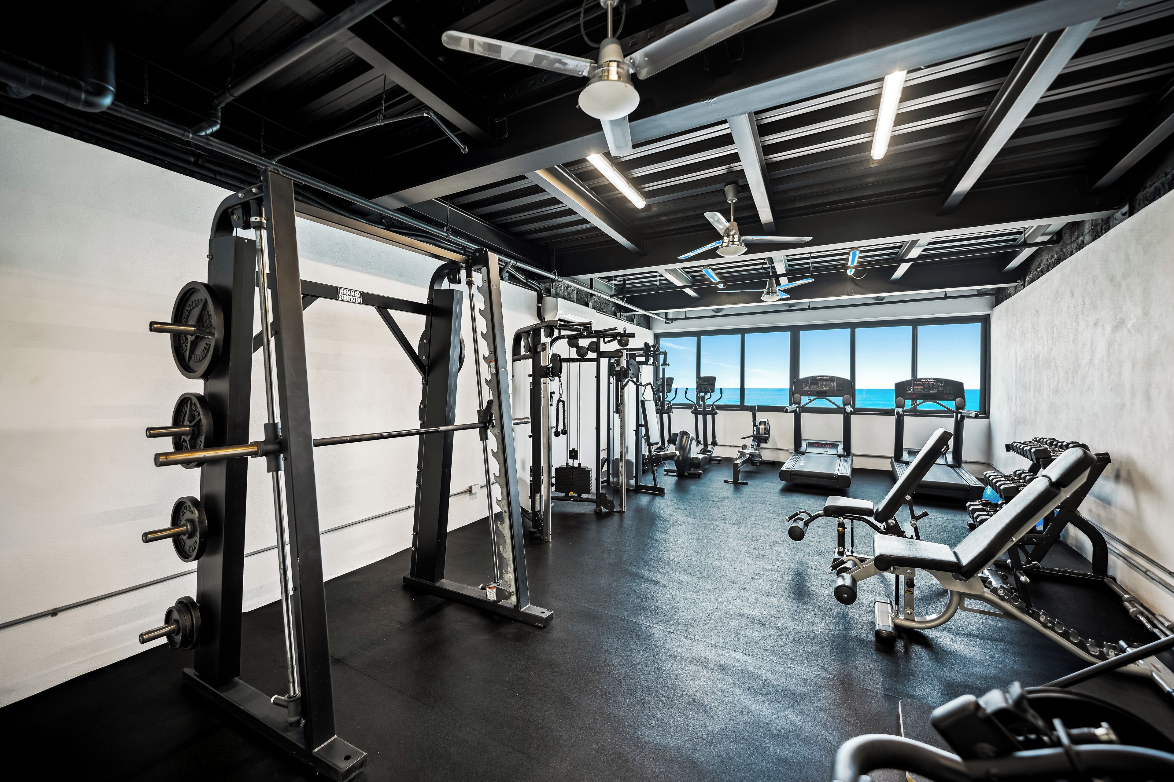 A gym with various exercise equipment, a ceiling fan, and large windows offering a view.