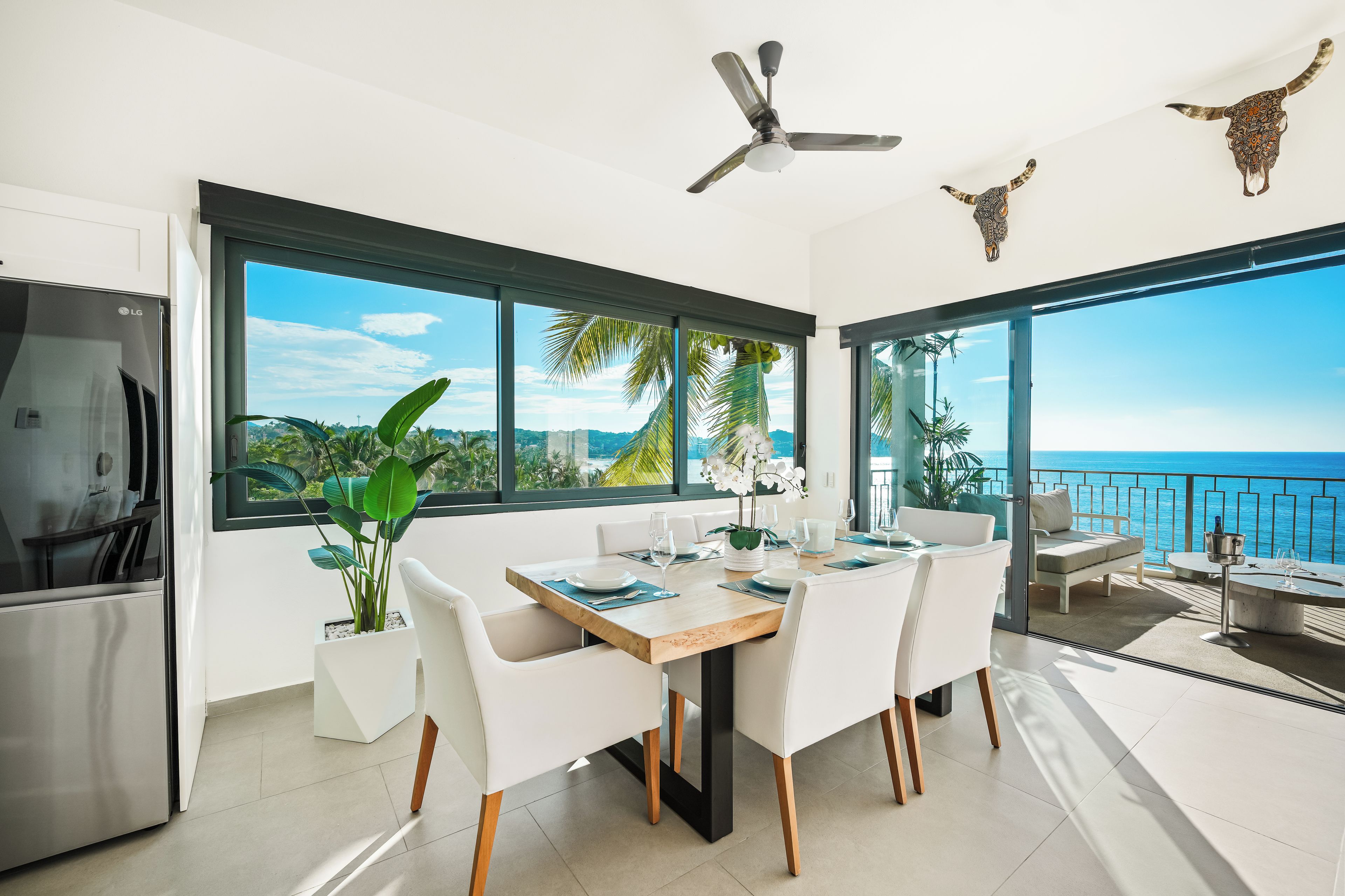 Uma área de refeições moderna com vista para o mar, ventoinha no teto e arte decorativa na parede.