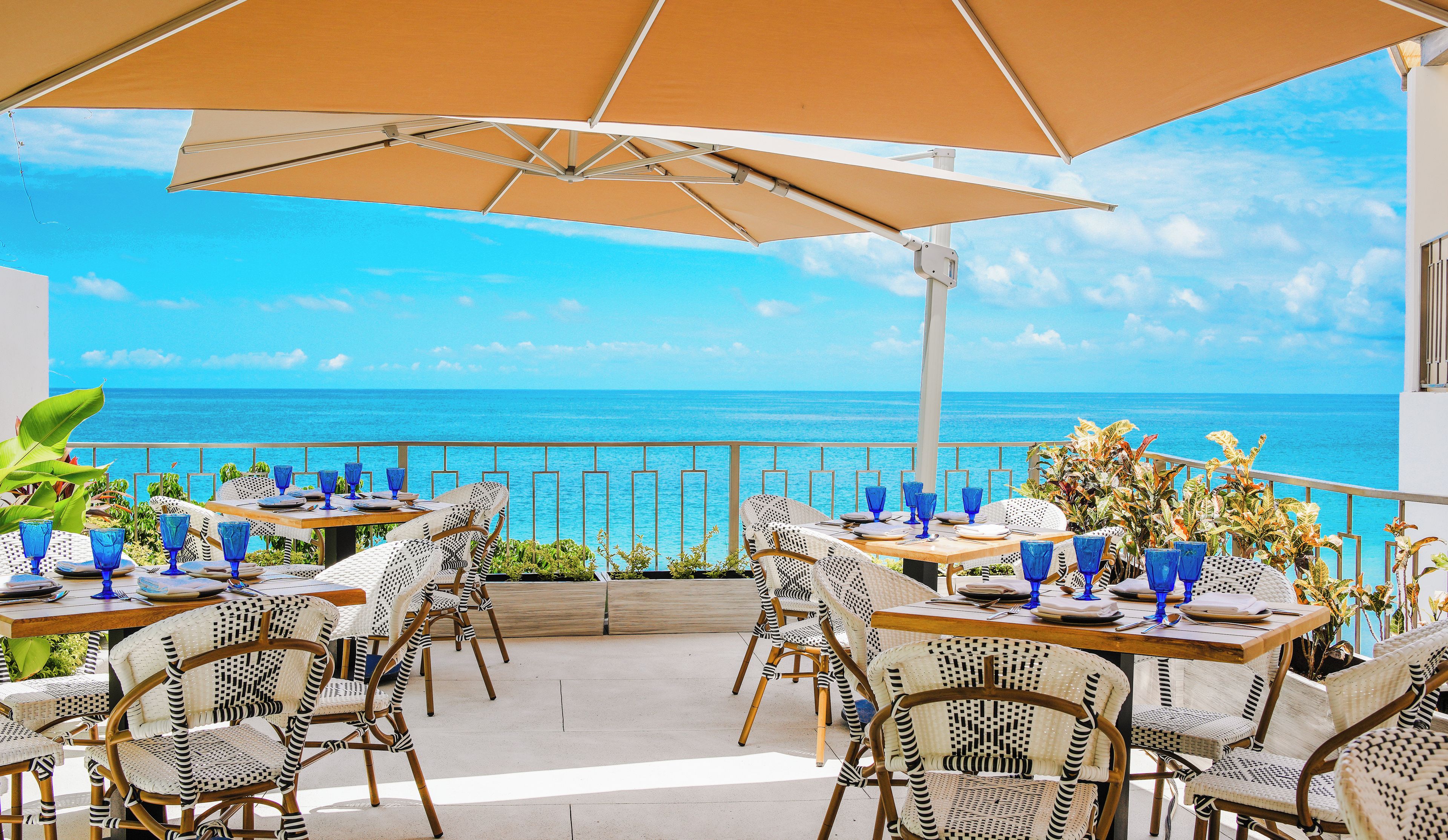 Un área de comedor al aire libre con mesas y sillas, con vista a un mar azul y transparente.