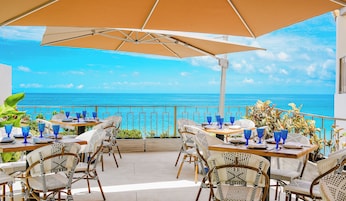 Un área de comedor al aire libre con mesas y sillas, con vista a un mar azul y transparente.