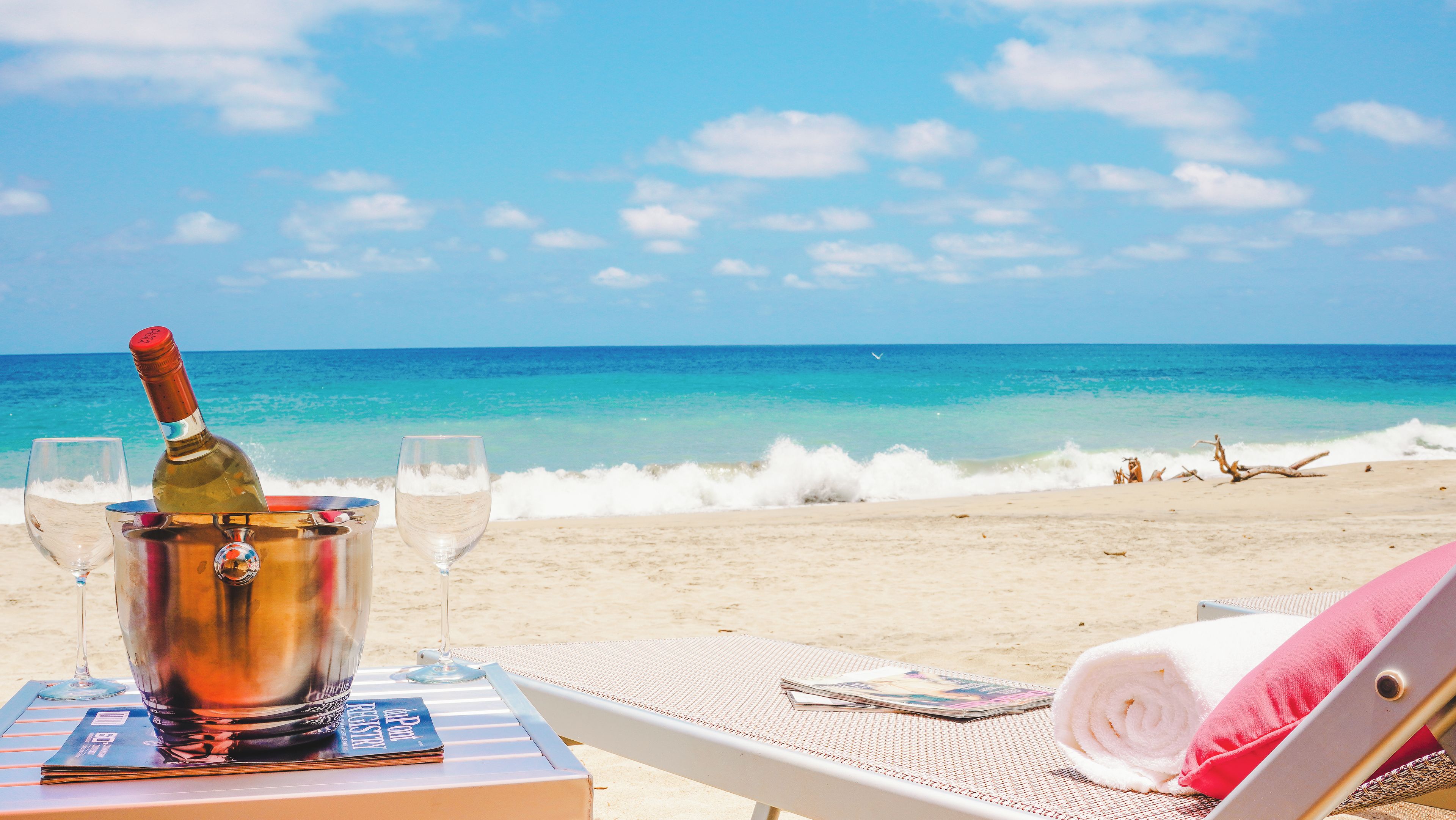 Una mesa en la playa con una botella de champán, copas y una revista.