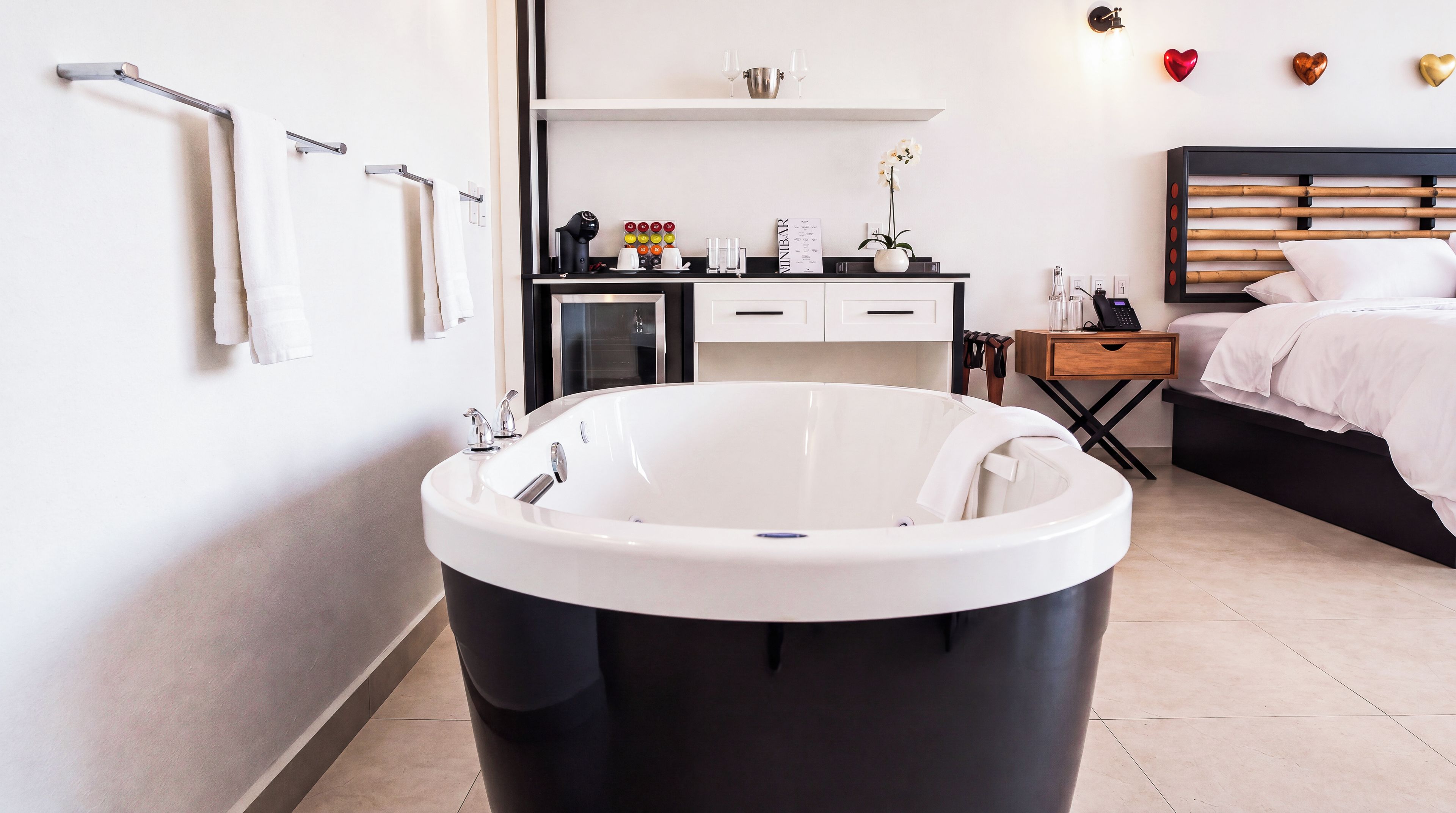 A modern bathroom with a freestanding bathtub, a vanity with a mirror, and a bed with a wooden headboard.