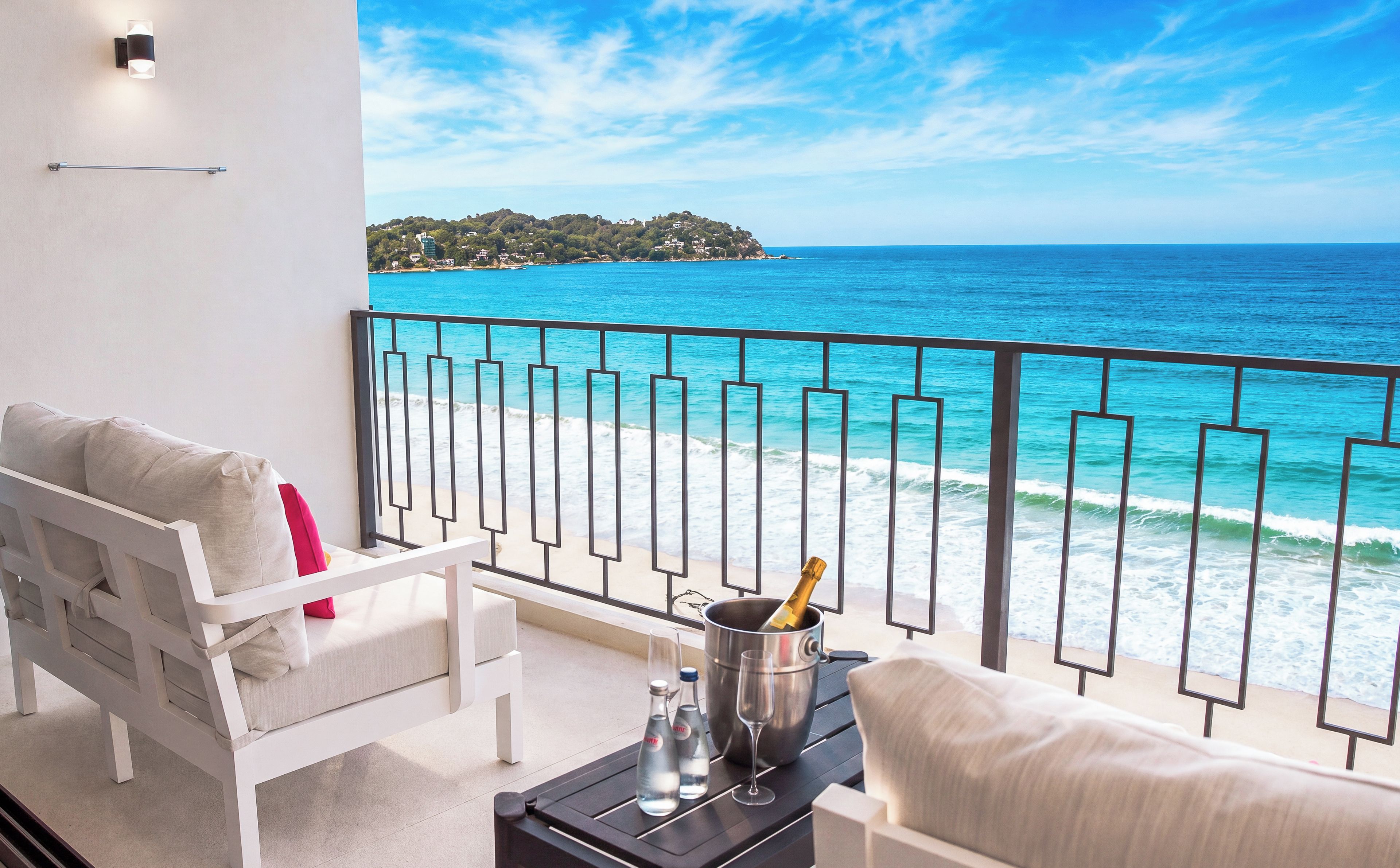 A balcony with a white sofa, a small table with a champagne bottle, and a view of the ocean.