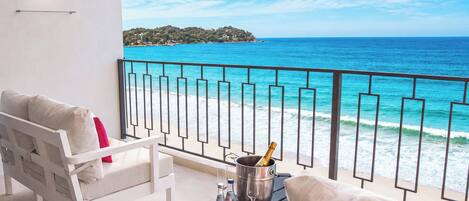 A balcony with a white sofa, a small table with a champagne bottle, and a view of the ocean.