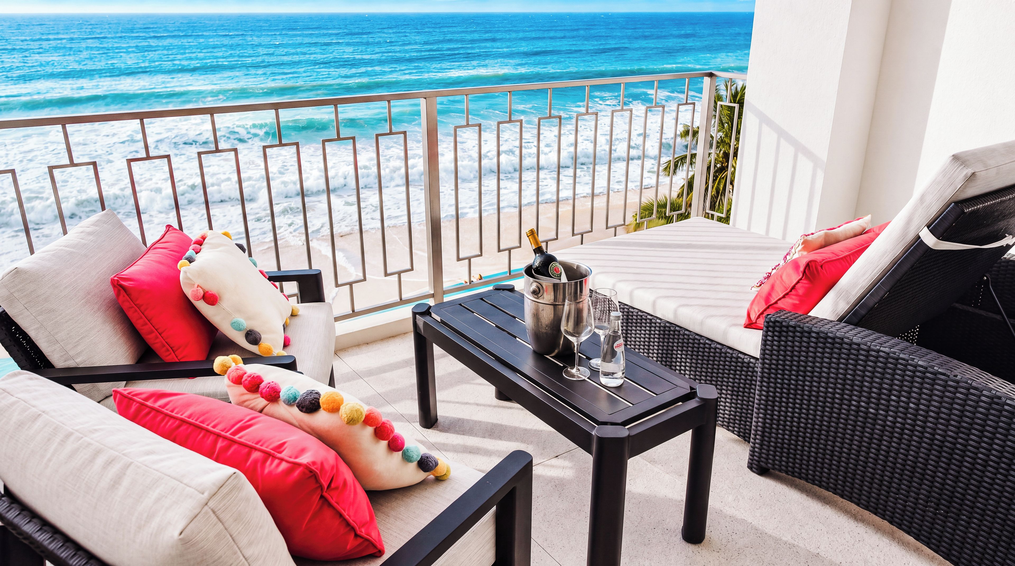 A balcony with a view of the ocean, furnished with a sofa, a table, and a bottle of champagne.