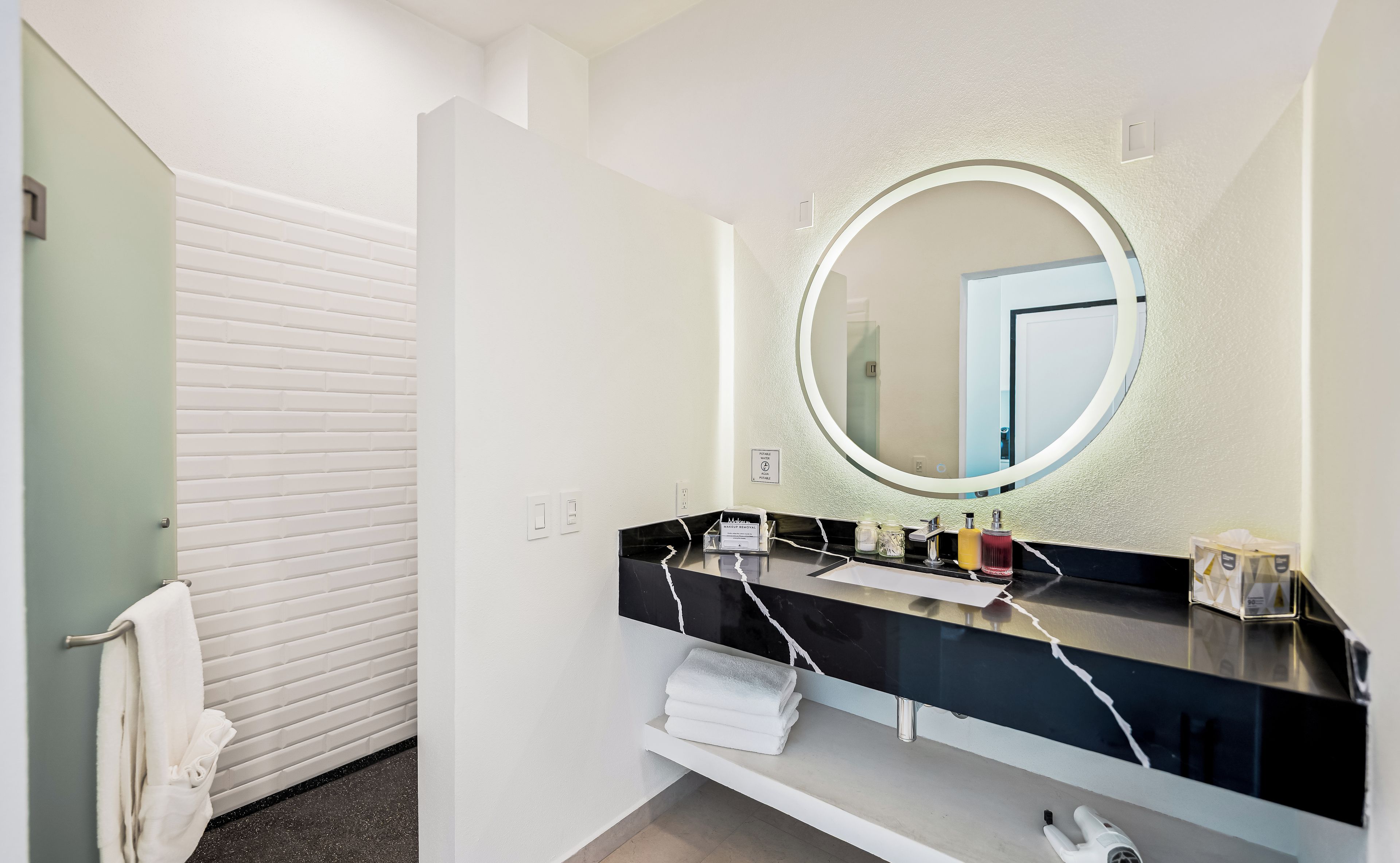 A bathroom with a white vanity, a round mirror, and a towel rack.