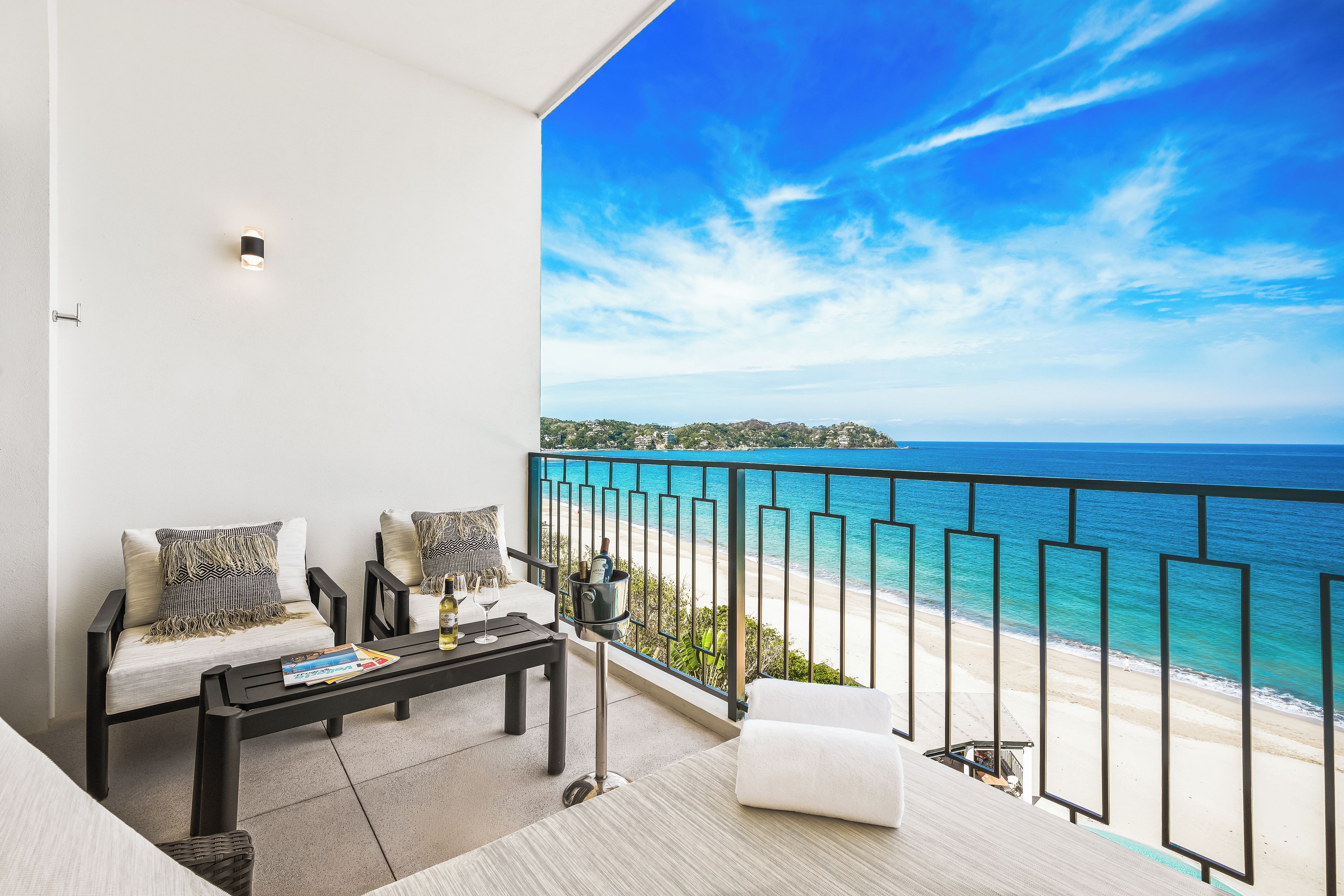 A balcony with a view of the beach and ocean, a sofa, a table, and a bottle of champagne.
