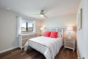 A bedroom with a bed, two nightstands, a ceiling fan, a window with curtains, and a view of the outside.