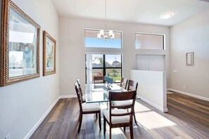 A dining area with a glass table, wooden chairs, a chandelier, and framed artwork on the walls.