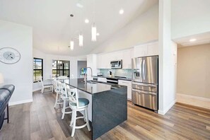 A modern kitchen with stainless steel appliances, a central island, and a dining area with bar stools.