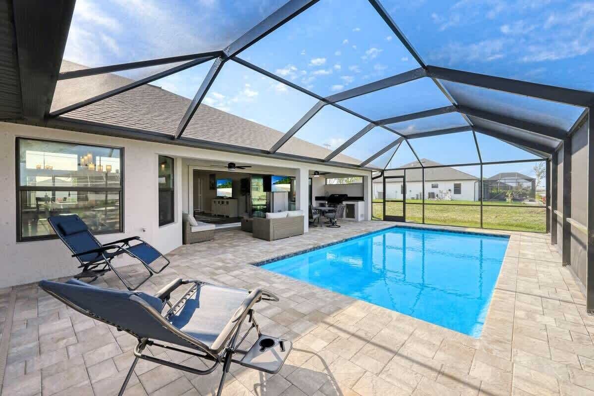 A covered outdoor swimming pool area with lounge chairs, a patio, and a view of the surrounding landscape.