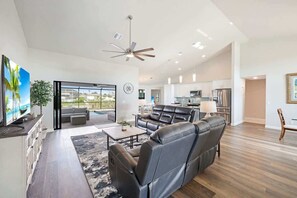 A modern living room with a leather sofa, a flat-screen TV, and a ceiling fan.