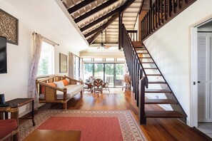A spacious living area with a wooden staircase, a sofa set, and a dining table.