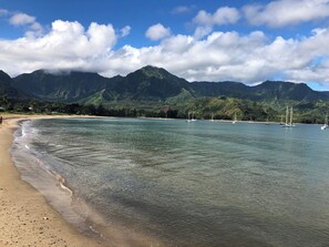 A beach with clear water, boats, and mountains in the background.