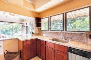 A kitchen with granite countertops, a dishwasher, and a window with a view of greenery.