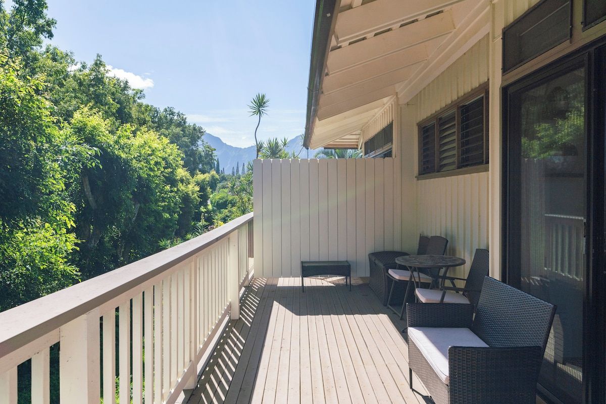 A balcony with a wooden floor, a white fence, and outdoor furniture including a sofa and chairs.