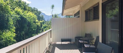 A balcony with a wooden floor, a white fence, and outdoor furniture including a sofa and chairs.