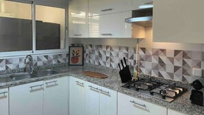 A modern kitchen with white cabinets, a granite countertop, a gas stove, and a window with blinds. - Superbe Appartement Familial à Hammamet Nord! (Nabeul‎)