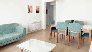 A modern living room with a sofa, a glass-top coffee table, and a dining area with chairs and a table. - Superbe Appartement Familial à Hammamet Nord! (Nabeul‎)