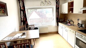 A kitchen with a dining table, chairs, a window with a view of a house, and a coffee maker. - Ferienwohnung Göss (Leoben)