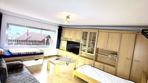 A spacious room with a large bed, a sofa, a TV, and wooden cabinets. - Ferienwohnung Göss (Leoben)