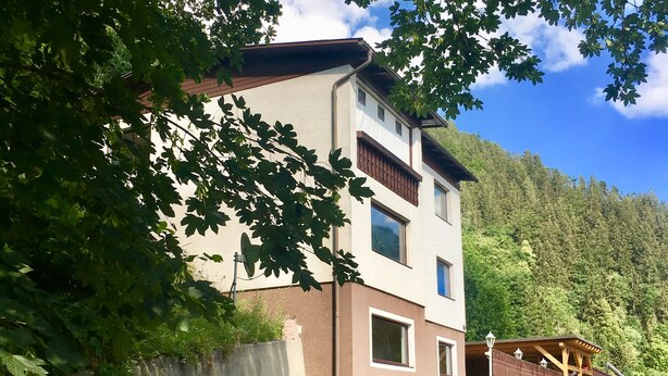A two-story building with a sloped roof, a satellite dish, and a small porch area. - Ferienwohnung Göss (Leoben)