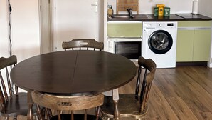 A dining area with a round table and wooden chairs, a washing machine, and a kitchen area with a sink and cabinets.