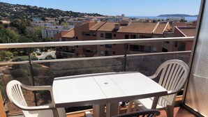 A balcony with a table and chairs, overlooking a residential area with buildings and a distant view of the sea.