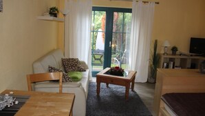 A cozy living room with a sofa, a coffee table, a TV, and a balcony with curtains. - Apartment Haubentaucher 600 meters from the beach (Prerow)