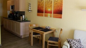 A compact kitchen with wooden cabinets, a microwave, and a dining area with a table and chairs. - Apartment Haubentaucher 600 meters from the beach (Prerow)