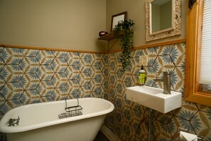 Une salle de bain avec une baignoire sur pieds, un lavabo avec un miroir au-dessus et un mur recouvert de carreaux décoratifs.