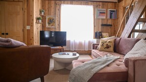 Ein gemütliches Holzhaus-Interieur mit Fernseher, zwei Sofas, einem Couchtisch und einem großen Fenster.