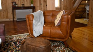 Ein brauner Ledersessel mit einer Decke und einem Kissen, ein Holzboden, ein gemustertes Teppich und eine Treppe im Hintergrund.