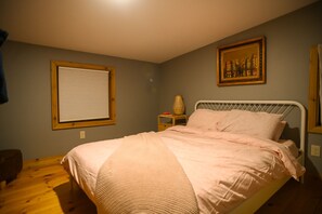 Une chambre avec un lit simple, une table de chevet, une lampe et un tableau encadré au mur.