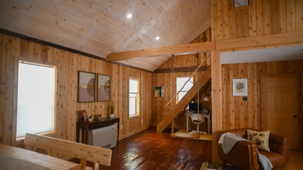 Ein Holzblockhaus-Interieur mit Essbereich, Wohnzimmer mit Sofa und Sessel, Treppe und einer kleinen Küchenzeile.