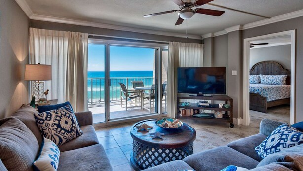 A spacious living room with a large TV, comfortable seating, and a balcony with a view of the ocean. - Beach House 304D - Gulf Front Condo (Miramar Beach)