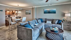 A living room with a grey sectional sofa, a coffee table, and a dining area with a kitchen in the background. - Beach House 304D - Gulf Front Condo (Miramar Beach)
