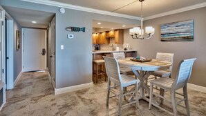 A dining area with a round table and four chairs, a kitchen with wooden cabinets, and a painting on the wall. - Beach House 304D - Gulf Front Condo (Miramar Beach)