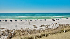 A beach with rows of umbrellas and beach chairs, a wooden fence, and a clear view of the ocean. - Beach House 304D - Gulf Front Condo (Miramar Beach)