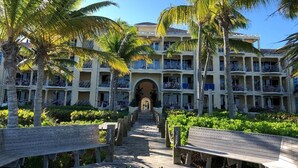 Un resort con un paseo central bordeado de palmeras, que conduce a un edificio de varios pisos con balcones.